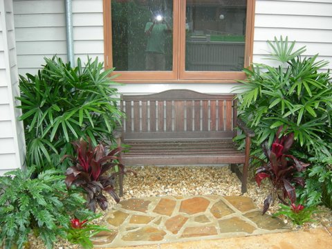 Timber garden bench framed by lush palms and cordylines above a crazy-paved path